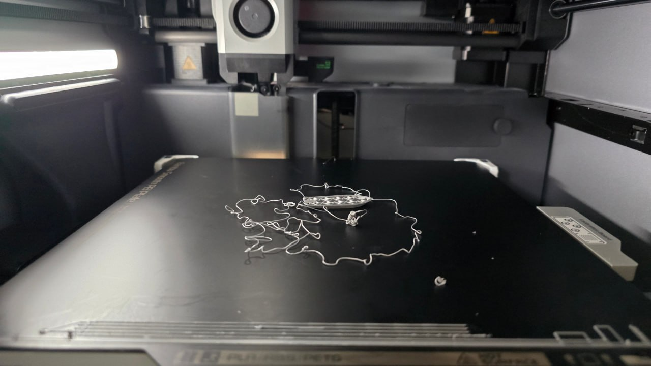 A failed first-layer print on a Bambu Lab X1C, the model popped off the bed leaving a tangled filament rat nest on the magnetic PEI plate