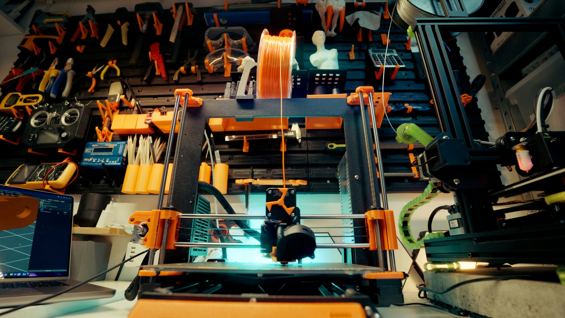 A 3D printer running in a workshop with tools and filament nearby